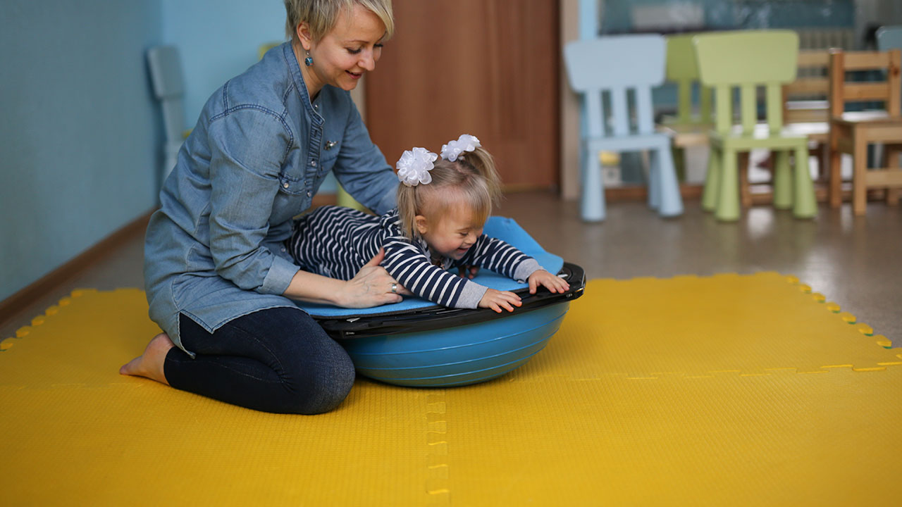 A physiotherapist helping a toddler balance on an exercise ball